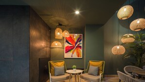 A modern lounge area with wicker chairs, a round table, and a large abstract painting. - Servatur Doña Elvira Adults Only (Mogán)