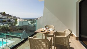 A balcony with a table set for two, overlooking a cityscape and a pool. - Servatur Doña Elvira Adults Only (Mogán)