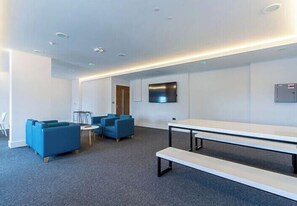 Una stanza moderna e luminosa con un tavolo grande e panche, posti a sedere blu e una televisione a schermo piatto appesa al muro.
