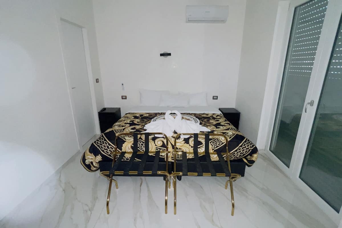 A bedroom with a bed, a nightstand, a wall-mounted light, and a sliding glass door.