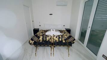 A bedroom with a bed, a nightstand, a wall-mounted light, and a sliding glass door.