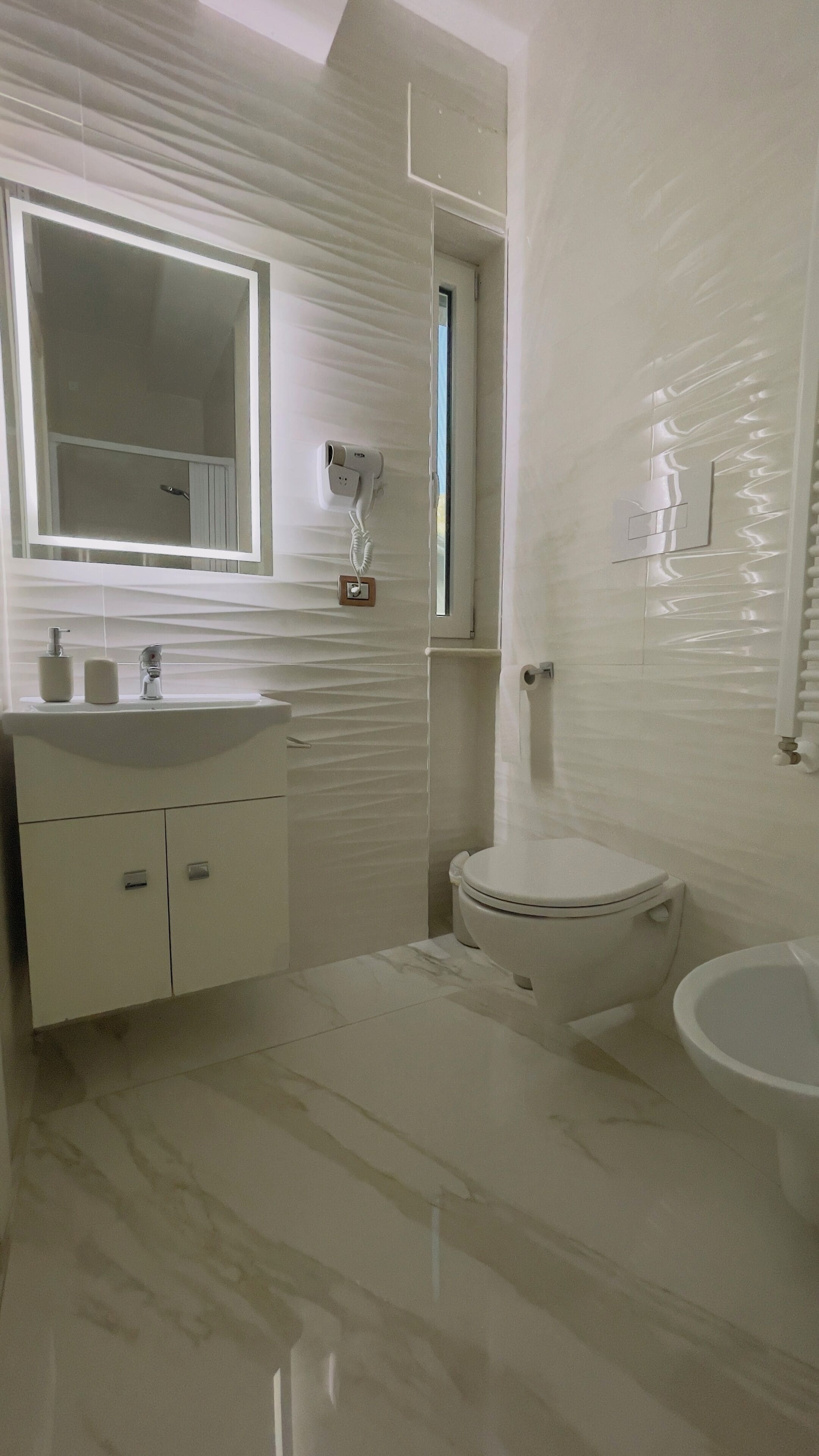 A modern bathroom with a white vanity, a large mirror, a toilet, and a bidet.