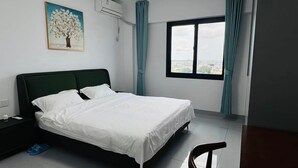 A neatly made bed in a room with a large window and a painting on the wall.