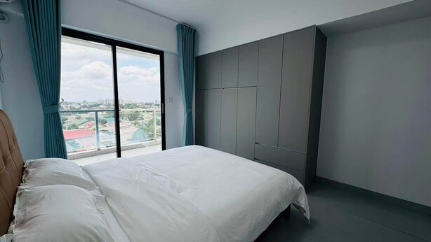 Ein Schlafzimmer mit einem großen Bett, einem Kleiderschrank und Blick auf eine Stadtlandschaft durch ein Fenster.