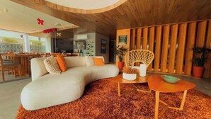 A modern living room with a curved sofa, a round wooden coffee table, and a textured rug. - W Tambaú Apart Hotel (João Pessoa)