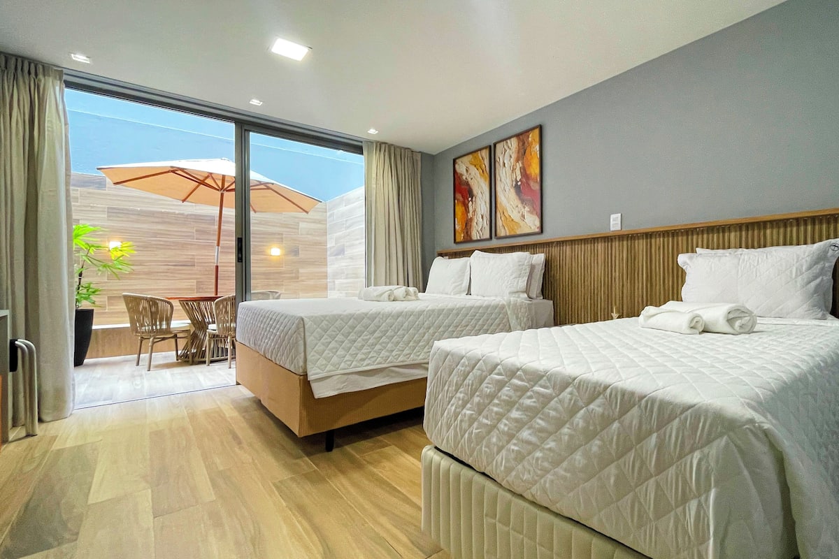 Habitación de hotel con dos camas, zona de comedor y vistas al exterior.