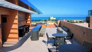 A rooftop terrace with outdoor seating, a barbecue area, and a view of the ocean. - W Tambaú Apart Hotel (João Pessoa)