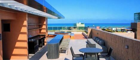 A rooftop terrace with outdoor seating, a barbecue area, and a view of the ocean.