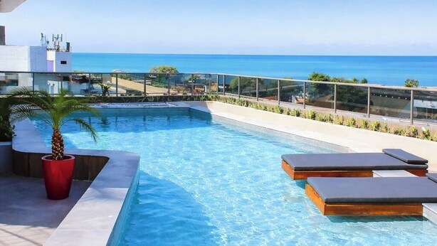 A modern swimming pool with clear blue water, lounge chairs, and a view of the ocean. - W Tambaú Apart Hotel (João Pessoa)