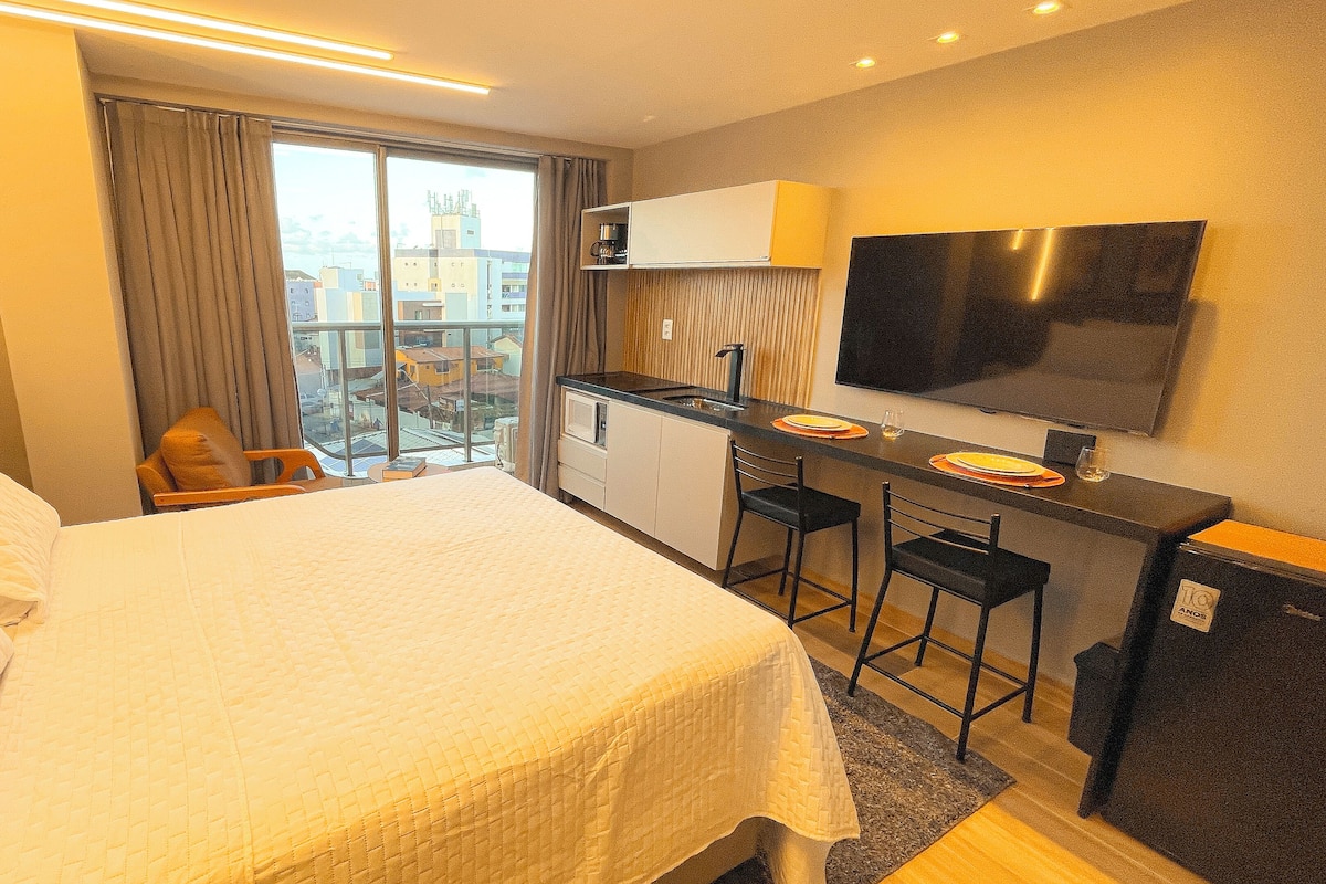 Habitación de hotel con cama, escritorio con dos sillas, televisión y vista a la ciudad por la ventana.