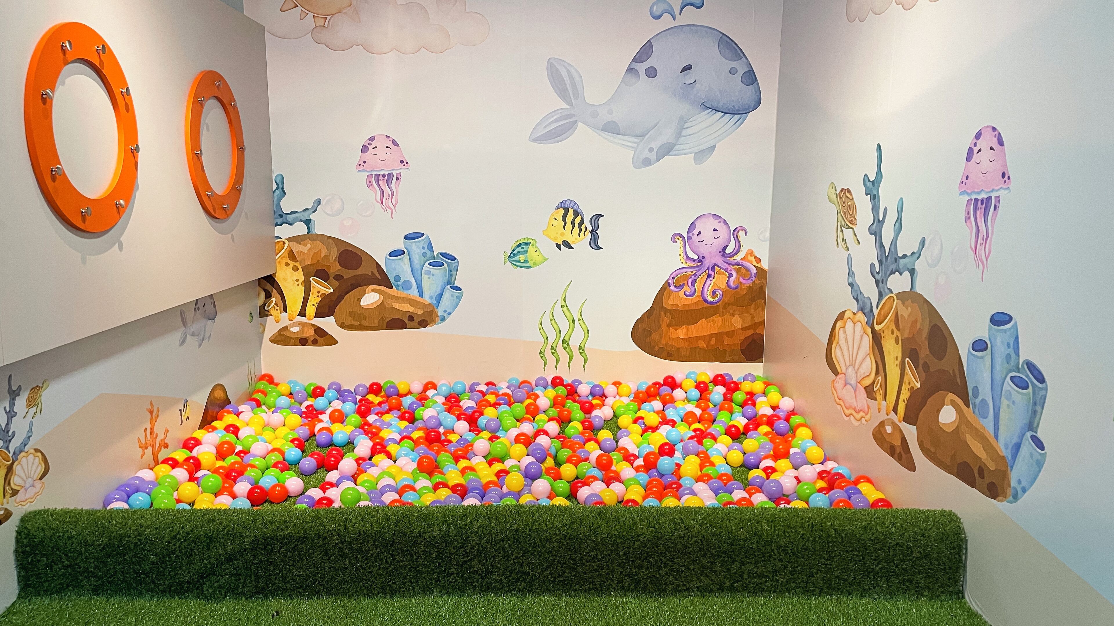 Uma área de recreação infantil com bolas coloridas, um mural de baleia e arte com polvos.