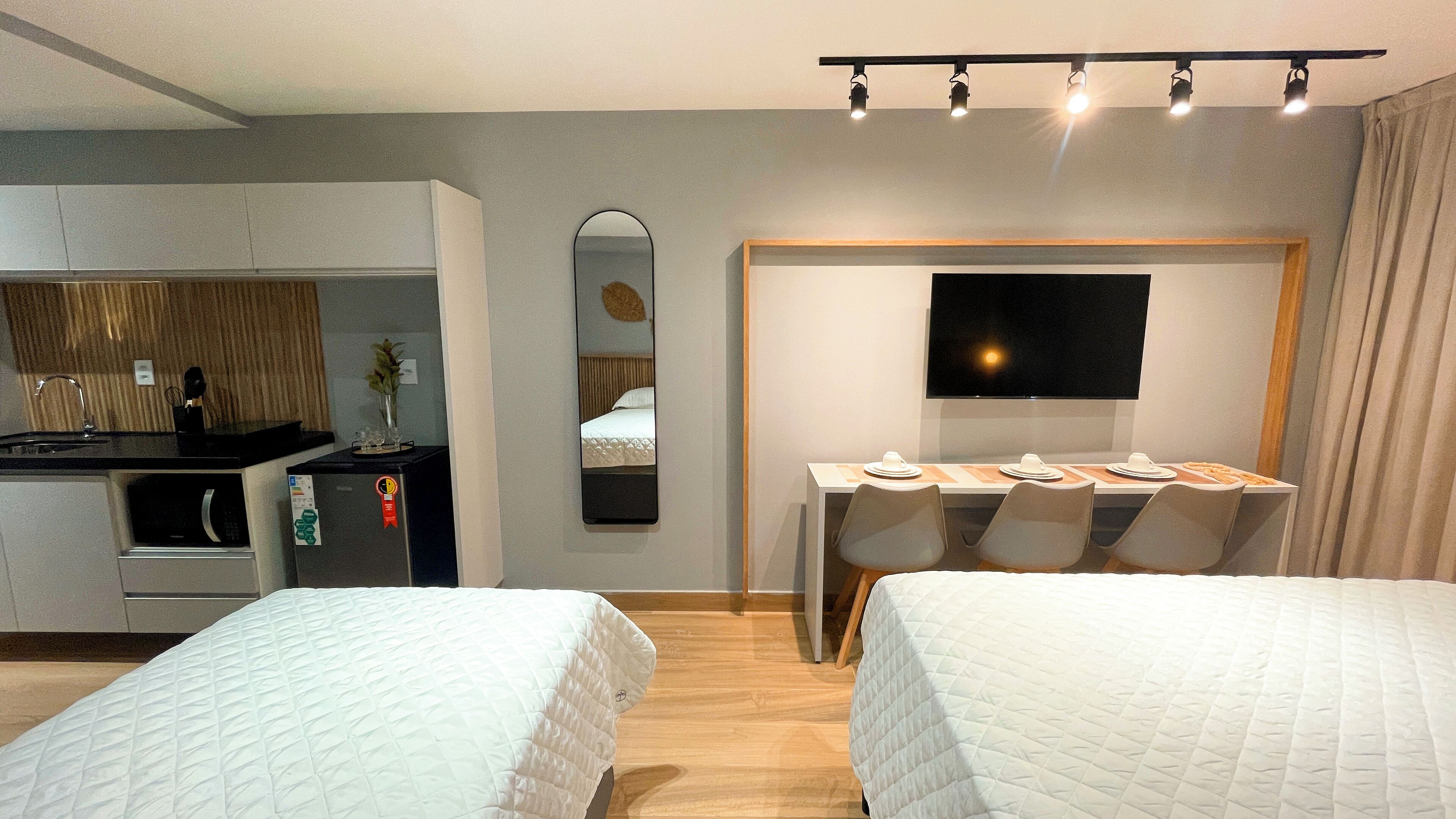 Une chambre d’hôtel avec deux lits, une kitchenette, un coin repas avec un téléviseur et un miroir.