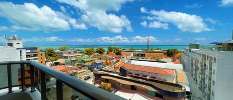 A coastal cityscape with a view of the ocean, buildings with red-tiled roofs, and a clear blue sky.