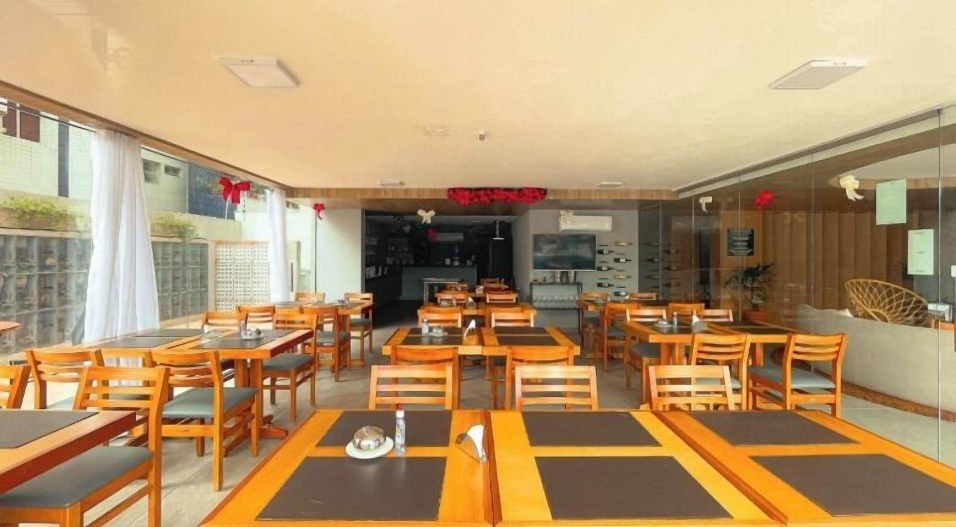 A restaurant with wooden tables and chairs, a kitchen area, and a view through glass walls.