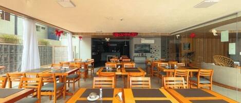A restaurant with wooden tables and chairs, a kitchen area, and a view through glass walls.