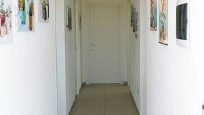Un couloir, avec une porte blanche au fond, et de part et d’autre des murs ornés d’œuvres d’art encadrées.