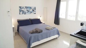 Een slaapkamer met een bed, een nachtkastje, een raam met gordijnen en een schilderij aan de muur.