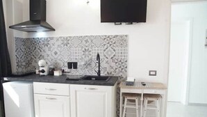 Een compacte keuken met witte kasten, een zwarte afzuigkap, een decoratieve spatwand en een kleine, witte koelkast.