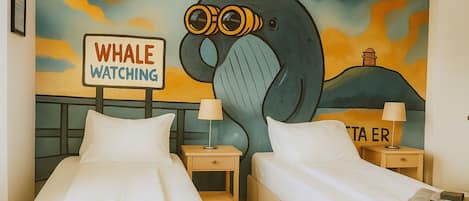 Habitación de hotel con dos camas, un mural de una ballena y un letrero que dice 'Avistamiento de ballenas'.