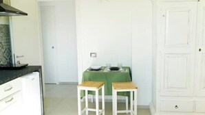 A kitchen with white cabinets, a black countertop, and a green tablecloth-covered table with two wooden stools. - Sirocco - House of Jana (Quartu Sant'Elena)