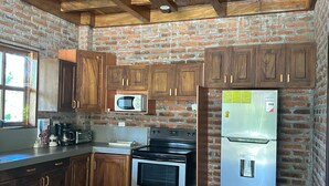 A kitchen with wooden cabinets, a microwave, a stove, and a refrigerator. - Rancho Tortuga Fuertevali (Acajutla)