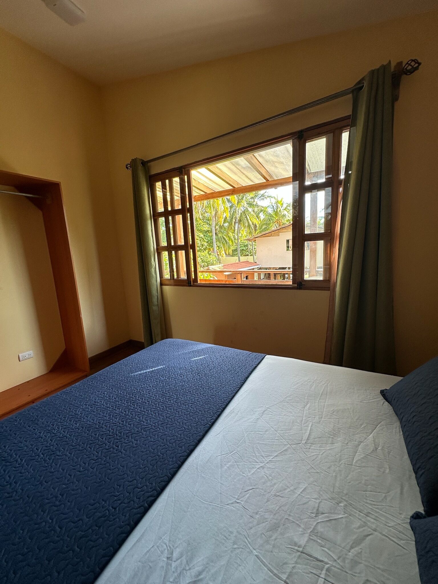 Un dormitorio con cama, ventana con cortinas y vistas al exterior.