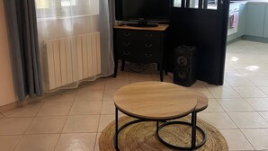 A living room with a television, a small table, and a kitchen area visible through an open door. - Beautiful studio (Volx)