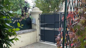A gated entrance with a concrete floor, surrounded by foliage and a metal fence. - Beautiful studio (Volx)