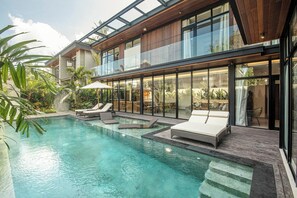 A modern house with a swimming pool, lounge chairs, and a glass-enclosed balcony. - Spacious 12BR Retreat 400m from Café Del Mar (Kuta Utara)