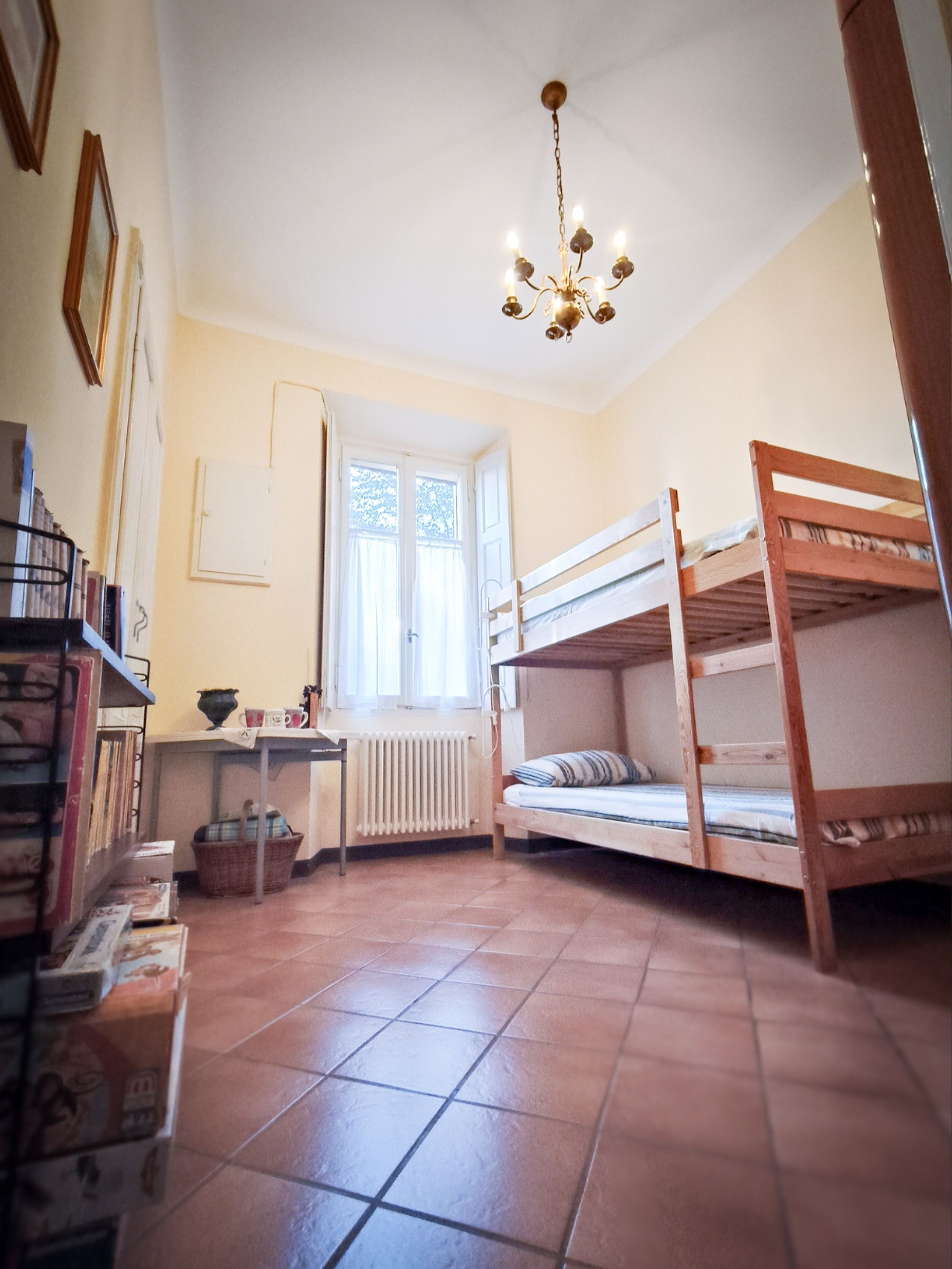 A dormitory room with bunk beds, a radiator, a window, and a chandelier.