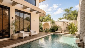 Ein moderner Poolbereich im Freien mit Holzterrasse, weißen Liegestühlen und einer Steinmauer.