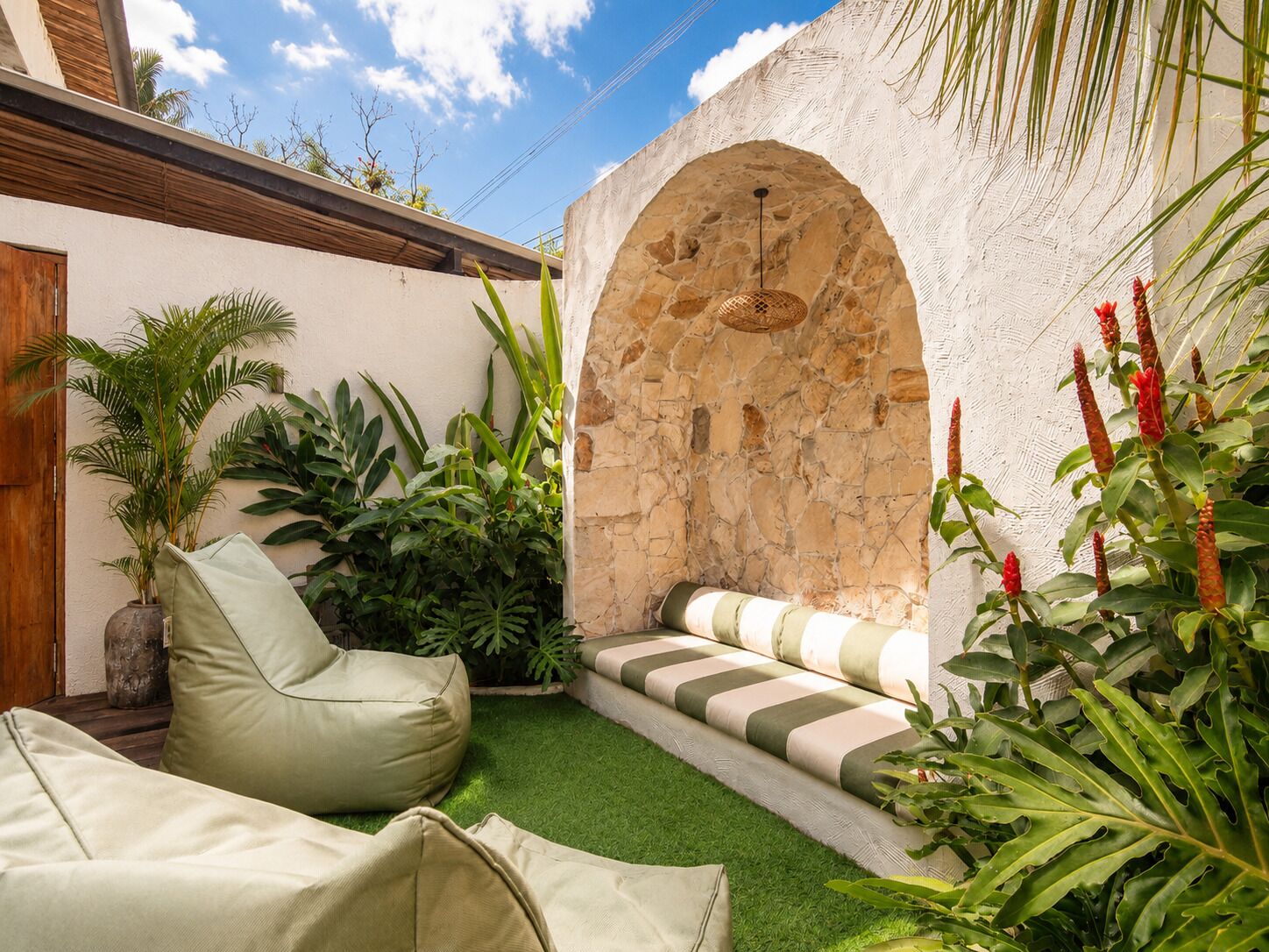 A courtyard with a stone wall, green artificial turf, a cushioned seating area, and various plants.