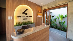 Una reception con pannello di legno sullo sfondo e un cartello con la scritta "The Kandra Ubud".