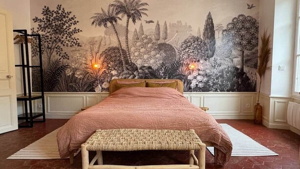 Une chambre avec un grand lit, un banc, une fresque murale et une échelle.
