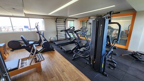 A gym with cardio machines, weightlifting equipment, and a mirror. - Lindo flat com varanda vista mar em João Pessoa (João Pessoa)