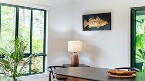 A dining area with a table, chairs, a lamp, and a framed fish artwork on the wall. - Beachside on Pacific (Mission Beach)