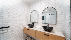 Ein Badezimmer mit weißen Fliesenwänden, zwei schwarzen Waschbecken, Holzschränken und einem schwarzen Handtuchhalter.