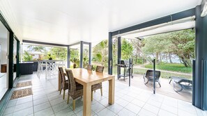 A spacious patio with a dining table and chairs, a grill, and a view of a lush garden. - Beachside on Pacific (Mission Beach)