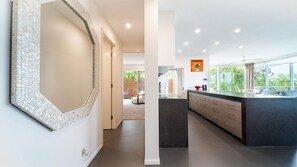 A modern kitchen with a large island, a dining area with a sofa, and a view of greenery outside. - Doorilla Coastal Retreat (Mission Beach)