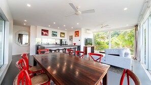 A modern kitchen with a dining area, a ceiling fan, and a large window with a view of greenery.
