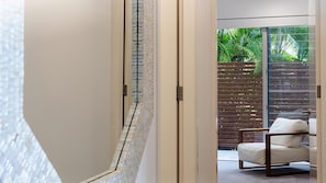 A modern interior with a sliding glass door leading to an outdoor area with a wooden fence and a cushioned chair. - Doorilla Coastal Retreat (Mission Beach)