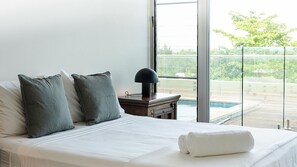 A hotel room with a bed, pillows, a nightstand, a lamp, and a view of a swimming pool through a glass door. - Doorilla Coastal Retreat (Mission Beach)