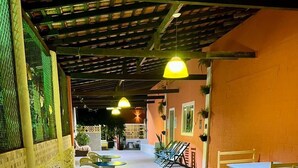 A covered outdoor seating area with round tables and chairs, a brick wall, and hanging lights. - Pousada Toa Toa Maruda (Marapanim)