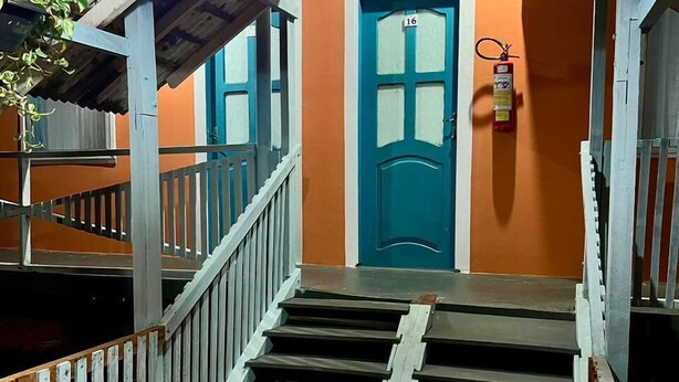 A wooden staircase leading to a door marked with the number 16, surrounded by orange walls and a blue door. - Pousada Toa Toa Maruda (Marapanim)