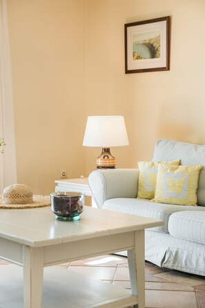 Ein Wohnzimmer mit einem weißen Sofa, einem Tisch mit einer Schüssel, einer Lampe und einem gerahmten Bild an der Wand.
