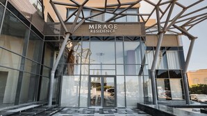 En modern byggnad med en skylt som visar texten ”MIRAGE RESIDENCE”. Den har stora glasfönster och en geometrisk metallkonstruktion ovanför entrén.