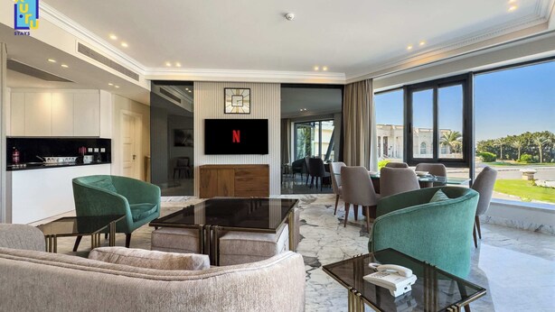 Ett modernt hotellrum med ett vardagsrumsutrymme som inkluderar en soffa, fåtöljer, ett soffbord och en TV som är monterad på väggen.