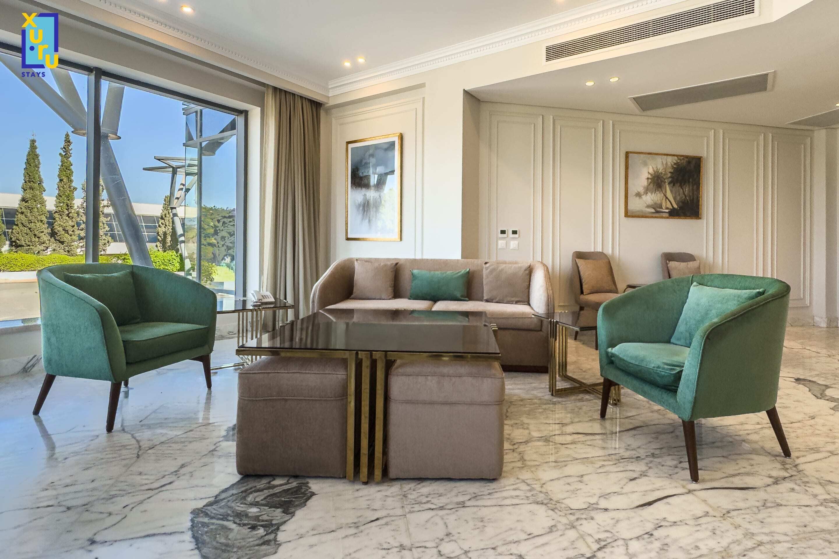 A spacious living room with a large window, a sofa set, two armchairs, and a coffee table.