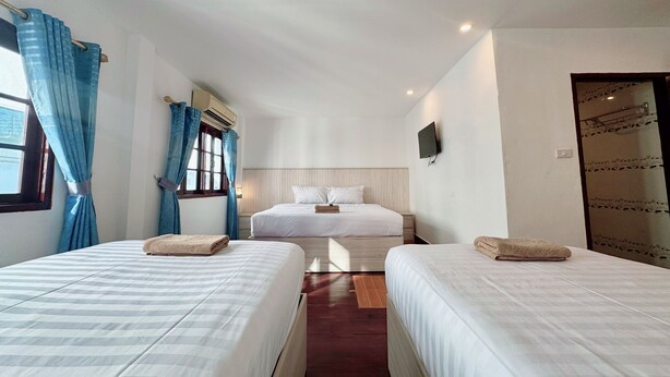 A hotel room with two beds, a large window with curtains, a flat-screen TV mounted on the wall, and a wooden floor. - Paradise Hostel  (Vang Vieng)