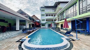 A swimming pool with lounge chairs and umbrellas, surrounded by buildings with balconies and windows. - Paradise Hostel  (Vang Vieng)